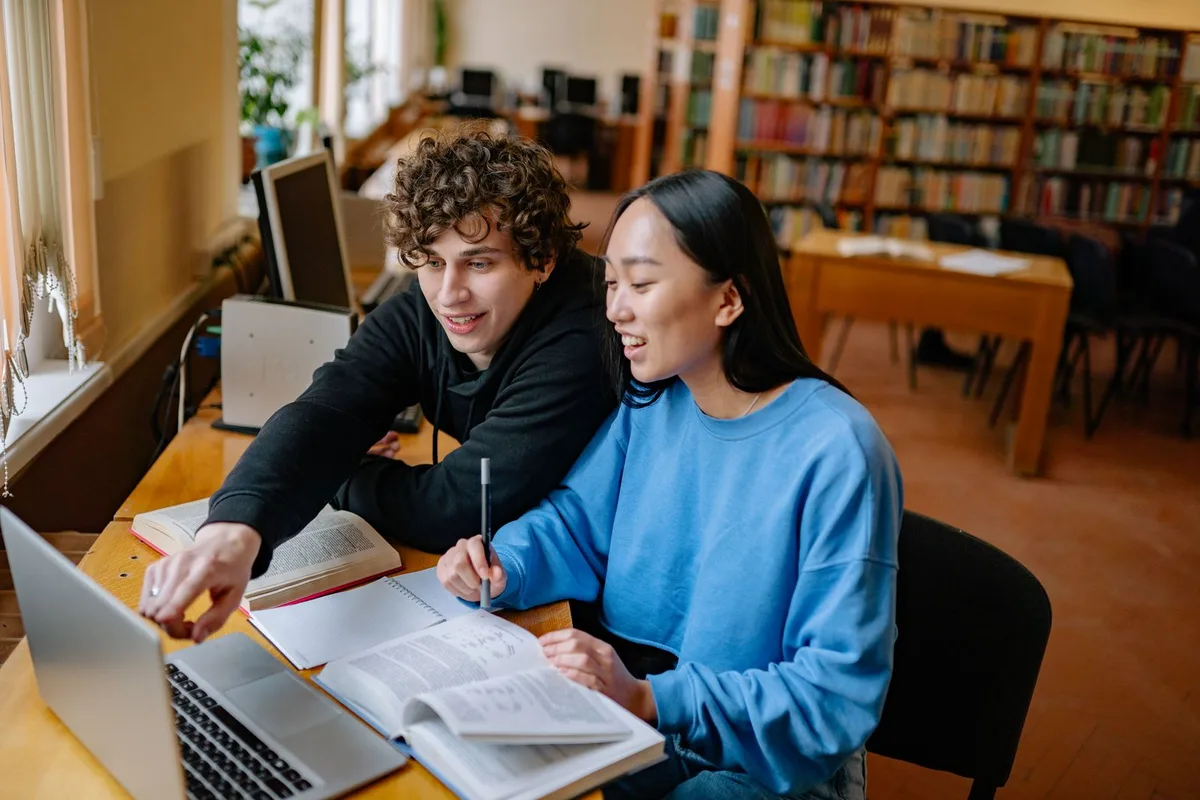 Two students reviewing information together on a laptop at a table in a college library