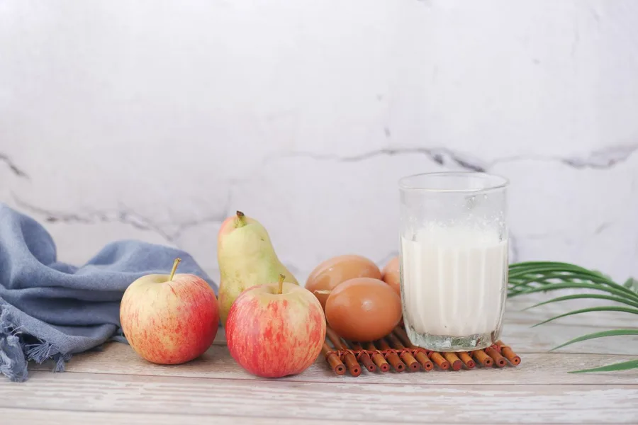 Apples, a pear, brown eggs and a glass of milk on a wooden table